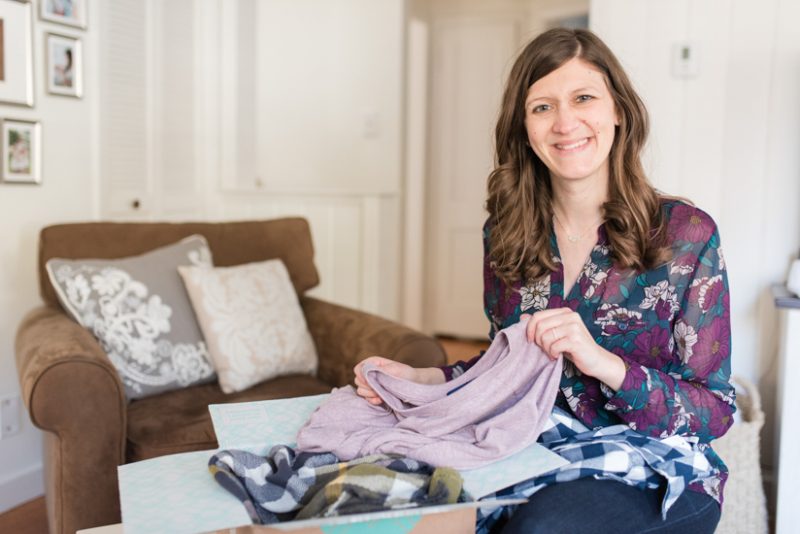 Woman holding Stitch Fix box with clothes inside to share a Stitch Fix review